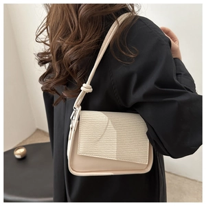 Detail view of a beige crossbody bag with textured flap and decorative shoulder knot