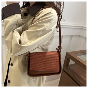 Close-up of a brown shoulder bag featuring an embossed woven flap and smooth leather texture