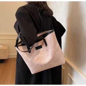 Detail of light pink tote bag with black handles being worn by a model in a warm room