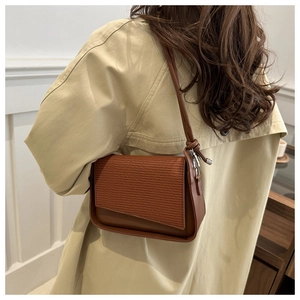 Detail of dark brown shoulder bag featuring woven texture flap and knotted strap detail