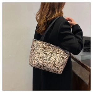 Detail of leopard print tote bag featuring a golden logo plate and black shoulder straps
