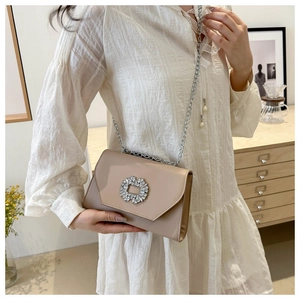 Detail of a beige crossbody bag featuring a rhinestone ring buckle and silver chain strap
