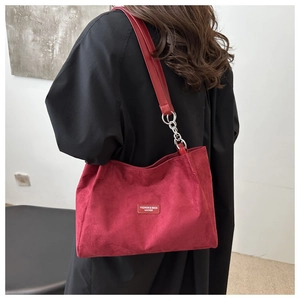 Detail view of deep red suede tote bag with metal chain strap on woman in black coat