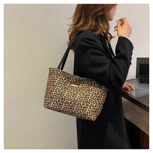 Detail of leopard print tote bag featuring a metal logo plate and slim black shoulder straps