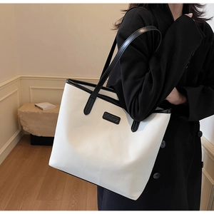 Detailed close-up of a large capacity cream tote bag with black trim on a model