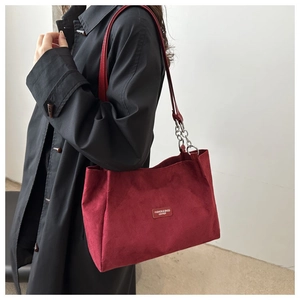 Detail of burgundy suede tote with leather chain strap on a black coat model