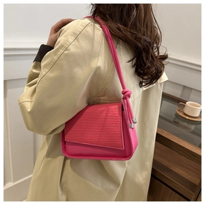 Detail of rose pink shoulder bag showing pleated texture and knotted strap with metal tips