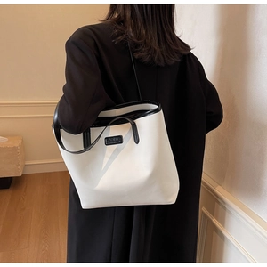 Minimalist white tote bag with black trim shown on a model in a warm home interior