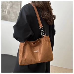 Detailed close-up of brown suede tote bag featuring silver chain straps and brand label