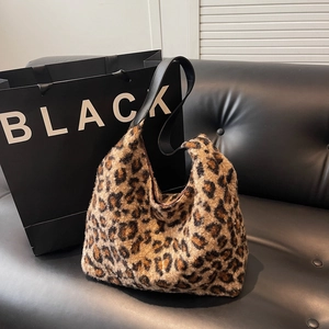 Chic leopard print plush hobo bag with black leather shoulder strap on a sofa