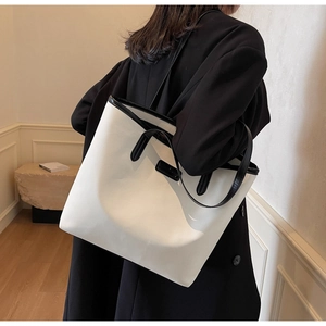 Detailed side view of large off-white tote bag with black straps on a woman's shoulder