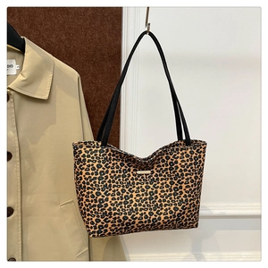 Close-up of leopard print tote bag with black shoulder straps and gold logo plate detail