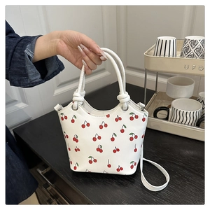 Close-up of a white leather tote bag with cherry print held by hand in a modern interior