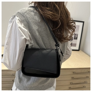 Macro view of black shoulder bag with textured leather flap and silver metal buckle