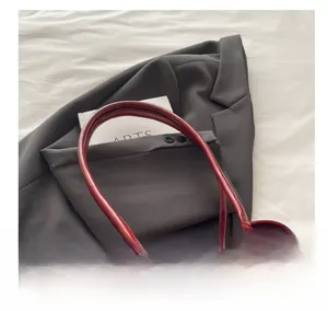 Detail of burgundy suede and patent leather handbag with metal rings on gray blazer