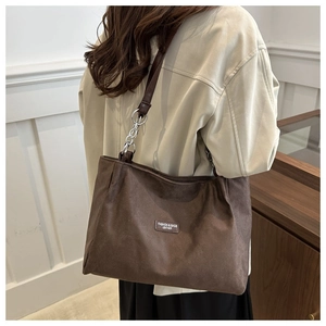 Detail of suede shoulder bag featuring a silver metal chain strap and minimalist leather tag