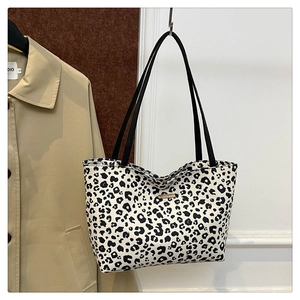 Detail of leopard print tote bag with black straps hanging next to a khaki trench coat