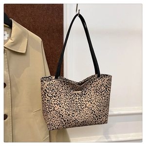 Detail of leopard print tote bag with black handles and metal logo plate on white wall