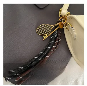 Detail of golden tennis racket keychain and woven tassels on a white leather bag
