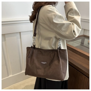 Detail view of large brown suede tote bag with metal chain strap and brand patch