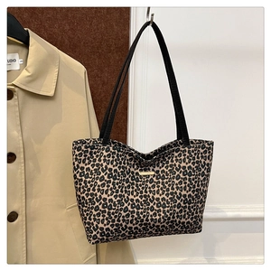 Detail of leopard print tote bag with black handles and gold logo on a studio hook