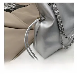 Detail showing the silver metallic bucket bag texture and chain strap on a trench coat