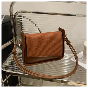 Detail of a brown leather shoulder bag with woven flap texture and knot strap accents