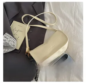 Detail of a beige faux leather baguette bag with metal tennis racket charm and silk scarf