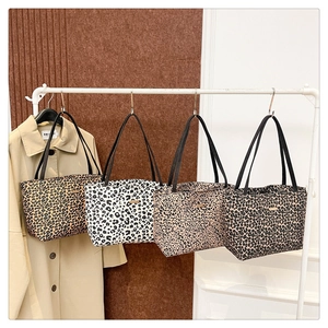 Detail of four leopard print tote bags in various colors on a display rack with a trench coat