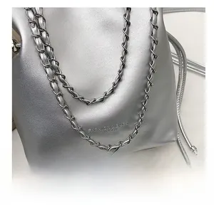 Close-up of silver textured bucket bag featuring metal chain and letter print detail