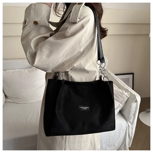Detail of minimalist black suede tote bag featuring a metal chain strap and leather label