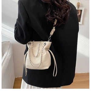 Detail view of cream chain bucket bag featuring metal drawstring closure and leather strap