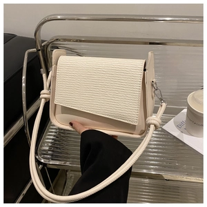 Close-up of cream textured flap handbag with metallic hardware in a modern setting
