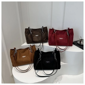 Detail showing assorted suede tote bags with chain straps on geometric white stands