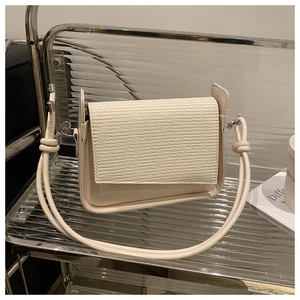 Detail of cream white shoulder bag featuring unique wavy textured flap and knotted strap
