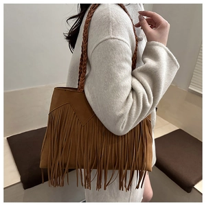 Close-up of brown suede bucket bag with long fringe tassels and woven strap details