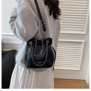 Side view of black bucket bag with silver chain and drawstring worn by a model