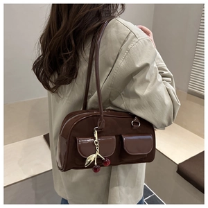 Close-up of brown suede shoulder bag featuring a decorative metal leaf and cherry charm