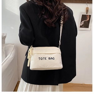 Detailed close-up of white corduroy tote bag featuring black embroidered TOTE BAG lettering