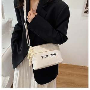 Beige corduroy crossbody bag with TOTE BAG embroidery and textured strap on a model