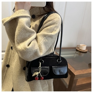 Detail of black suede shoulder bag with glossy trim and a red cherry charm accent