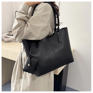 Detail of black pebbled leather tote bag with matching mini pouch on beige trench coat
