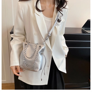 Detail of silver metallic bucket bag with adjustable strap and chain on a female model