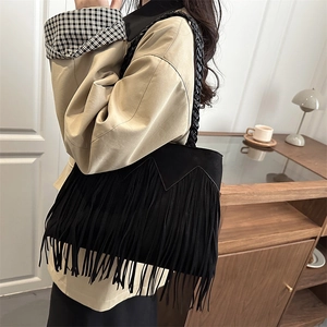 Chic black faux suede bucket bag with long tassels and woven strap on female model
