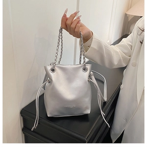Close-up of silver bucket bag with chain handle and drawstring closure held by model