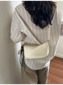 Detail showing cream crossbody bag with tennis racket charm and metal zipper