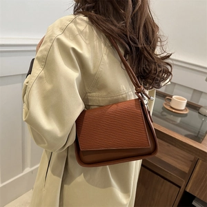 Brown textured shoulder bag with ripple flap design worn by a woman in beige coat
