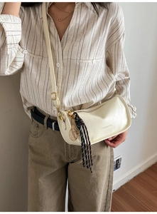 Detail of cream crossbody bag featuring golden tennis racket charm and woven strap accents
