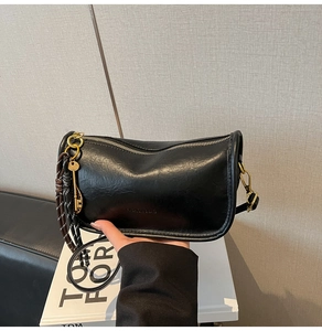 Detail of retro black leather shoulder bag featuring metal key charm and woven rope accent