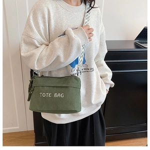 Detail of dark green corduroy tote bag featuring white embroidered text and woven strap